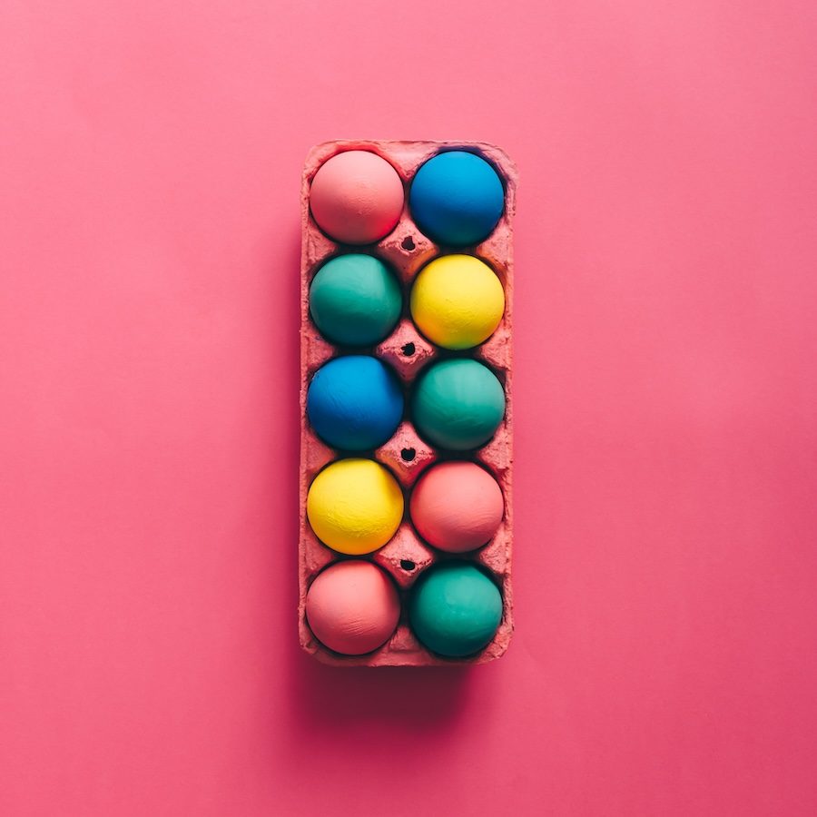 A carton of 10 colored eggs, arranged in two rows, on a pink background reflects the vibrant palette found in Singapore’s Digital Market, featuring pink, blue, green, and yellow hues.