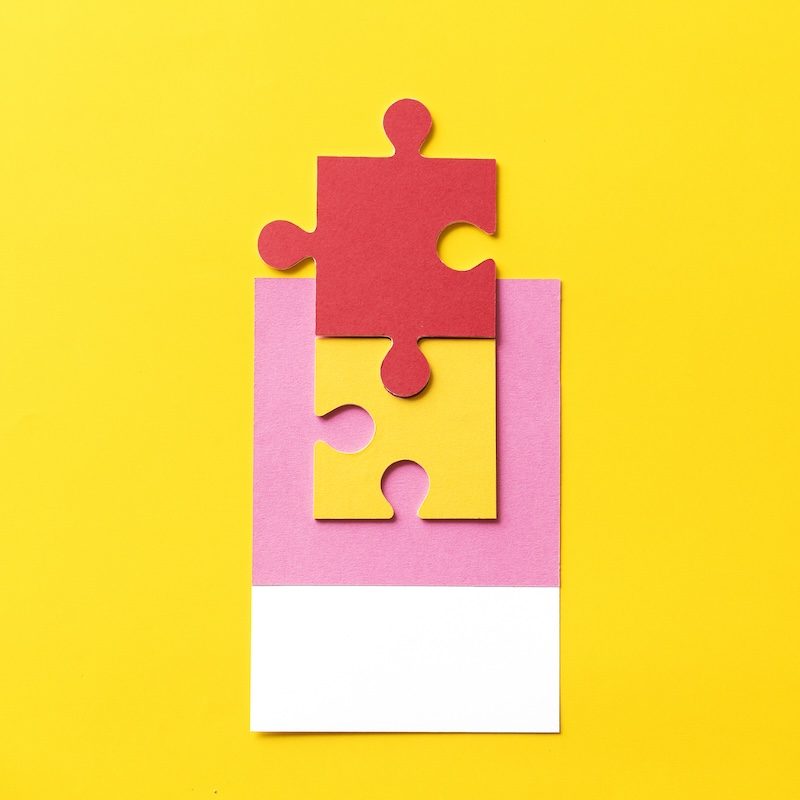 A red puzzle piece placed above a yellow puzzle piece, both positioned on a pink and white rectangular background set against a yellow backdrop, illustrating the seamless integration essential for an optimal website user experience.